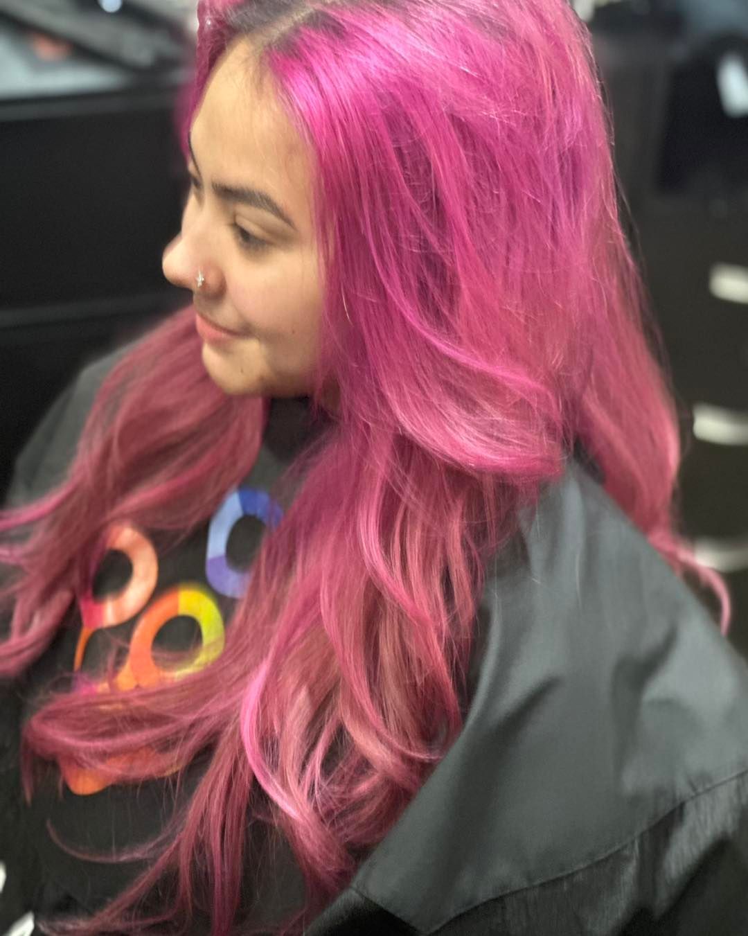 A woman with pink hair is sitting in a chair in a salon.