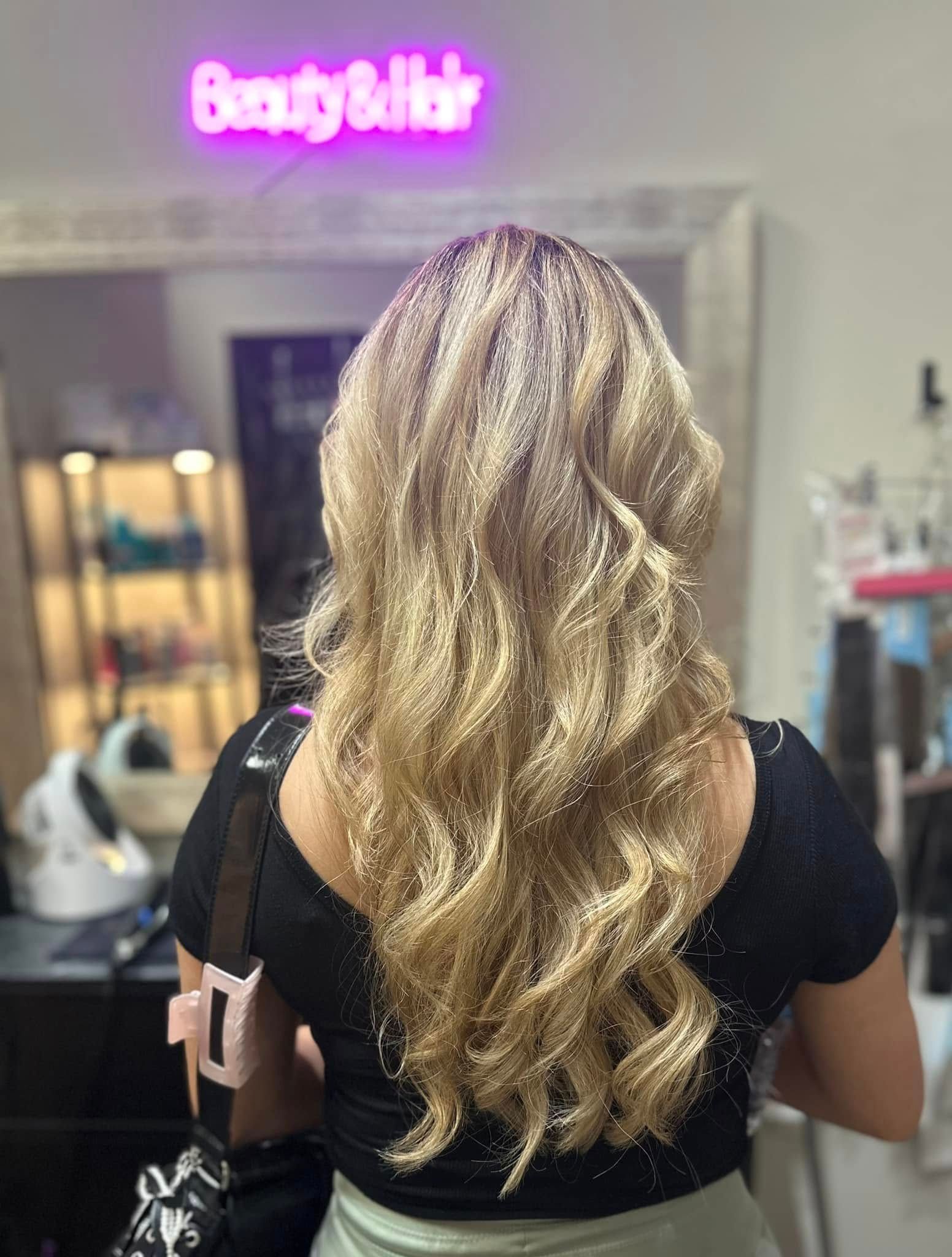 A woman with long blonde hair is standing in front of a beauty and hair sign.