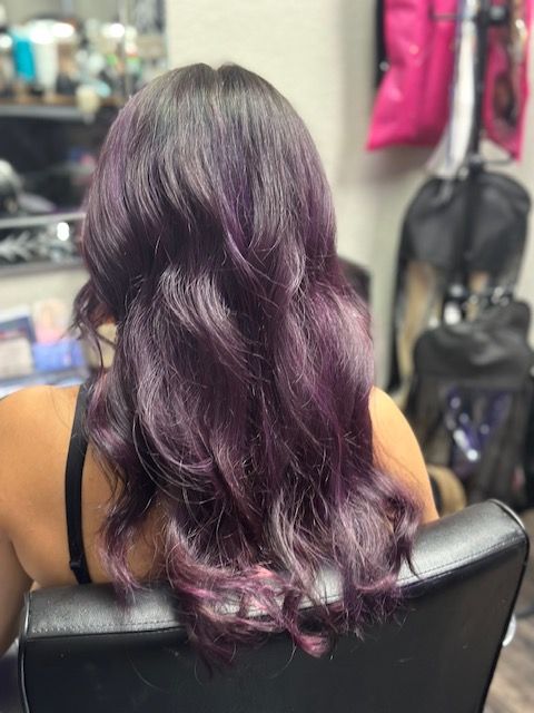A woman with purple hair is sitting in a chair in a salon.
