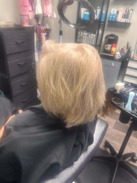 A woman is sitting in a chair in a salon getting her hair cut.