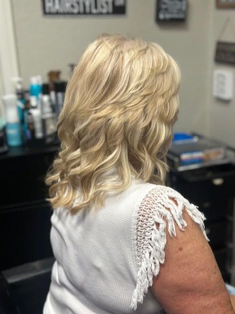 A woman with blonde hair is sitting in a chair in front of a sign that says hairstylist