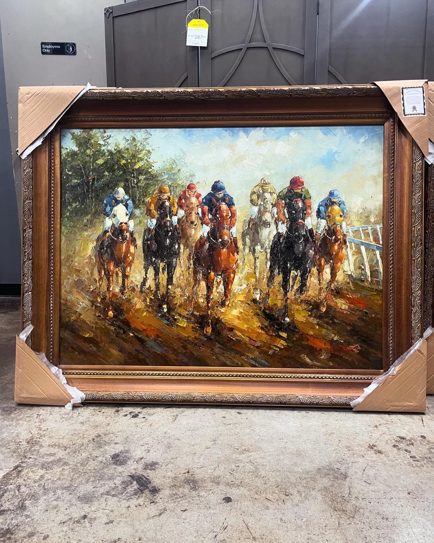 An oil painting in a gold frame depicts a group of jockeys racing horses on a dirt track.