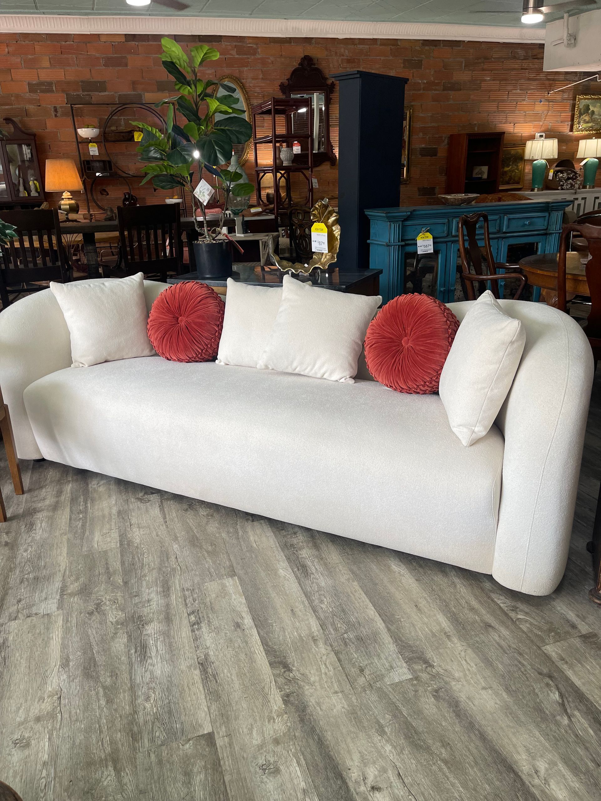 A cream-colored, curved sofa with textured fabric, adorned with four square cream pillows and two round red pillows.