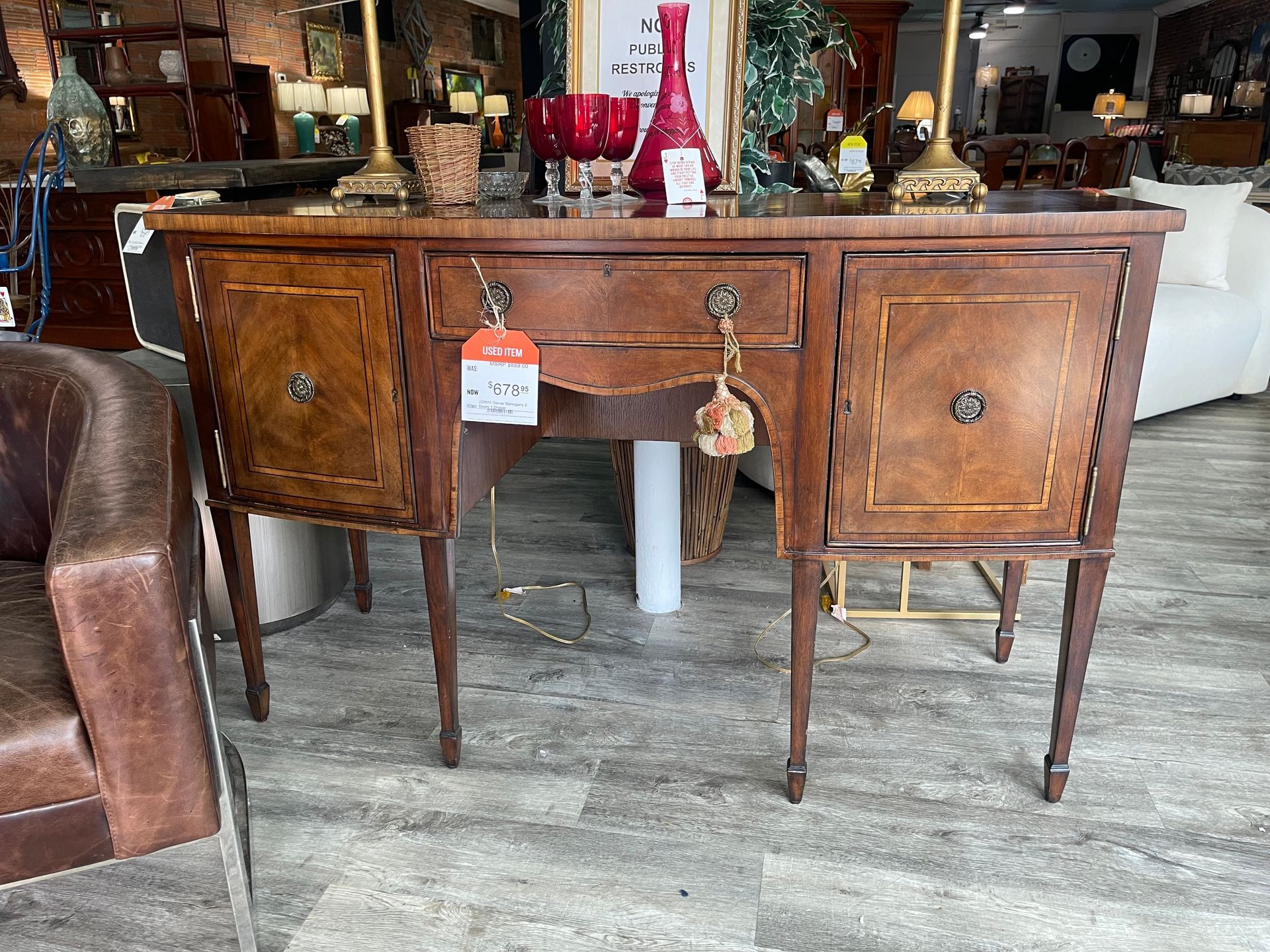 A vintage wooden sideboard featuring inlaid wood designs, two side cabinets, and a central drawer in a retail setting.
