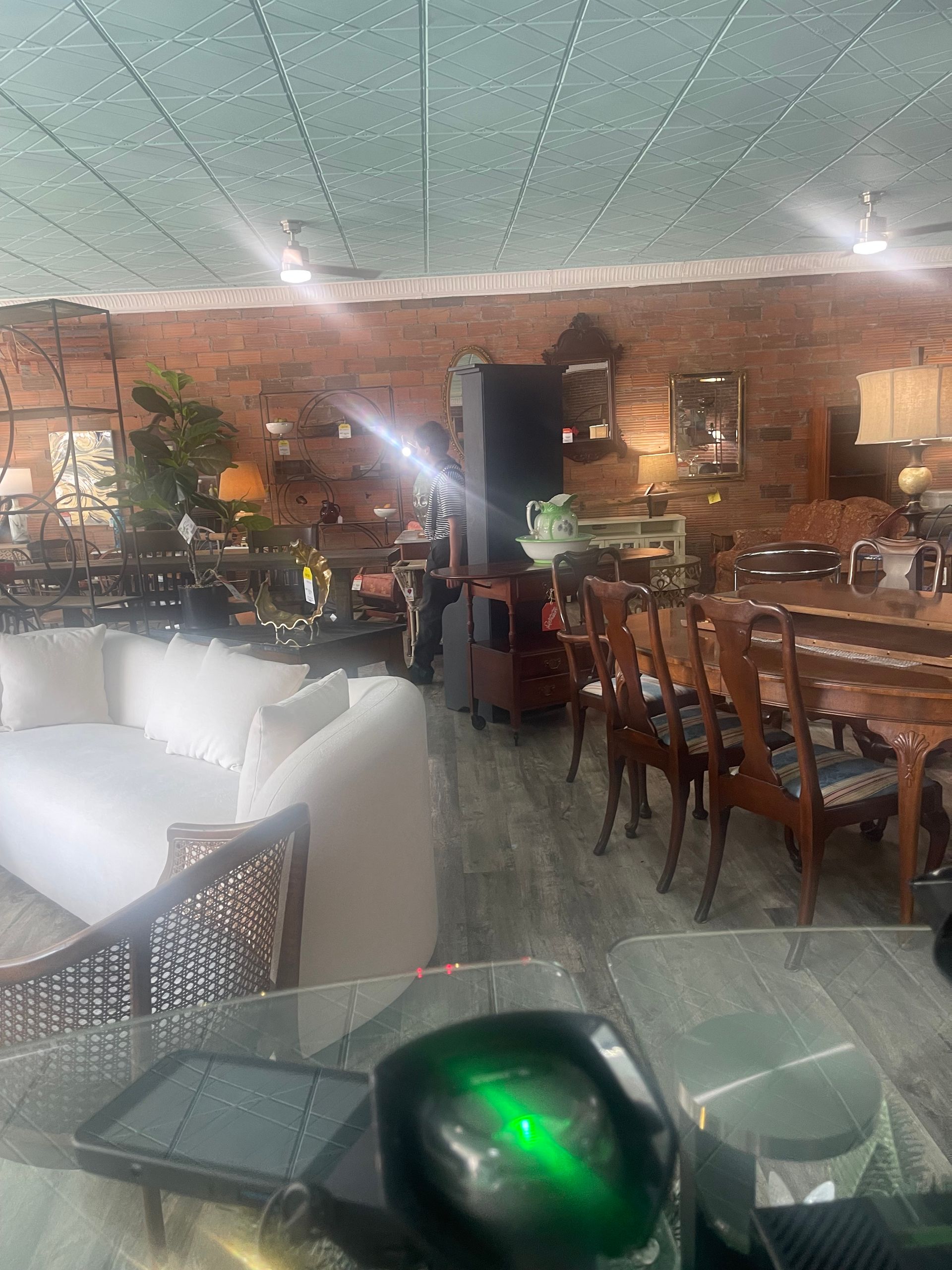 A furniture showroom with exposed brick walls, a white sofa in the foreground, and a dining table set in the back.