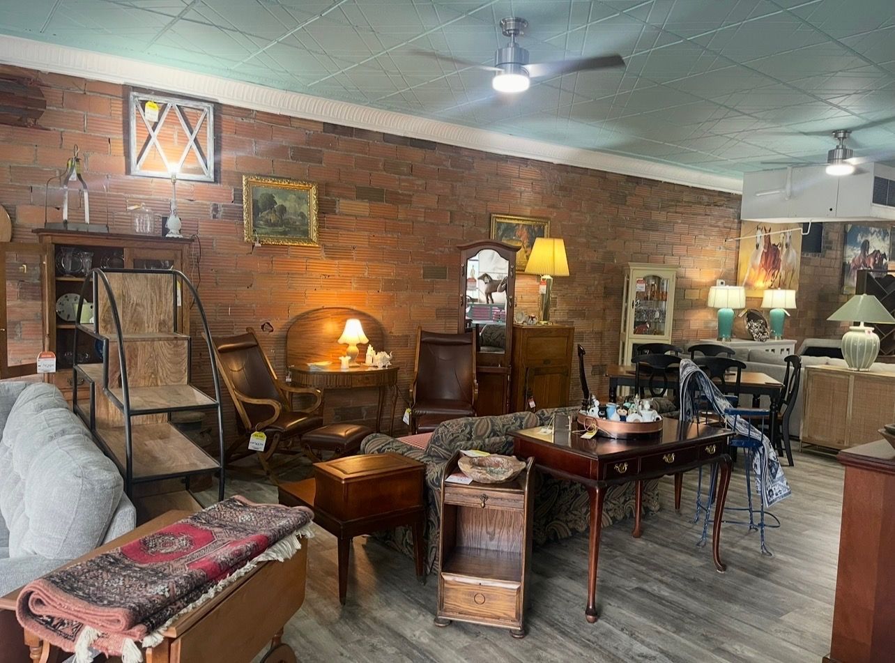 An antique store showroom featuring brick walls, wooden furniture, lamps, and a patterned rug on a sofa.