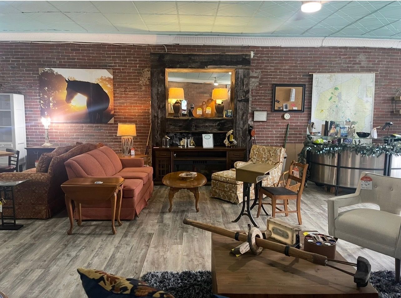 A showroom features a coral sofa, a dark wood coffee table, armchairs, and a large mirror against a rustic brick wall.