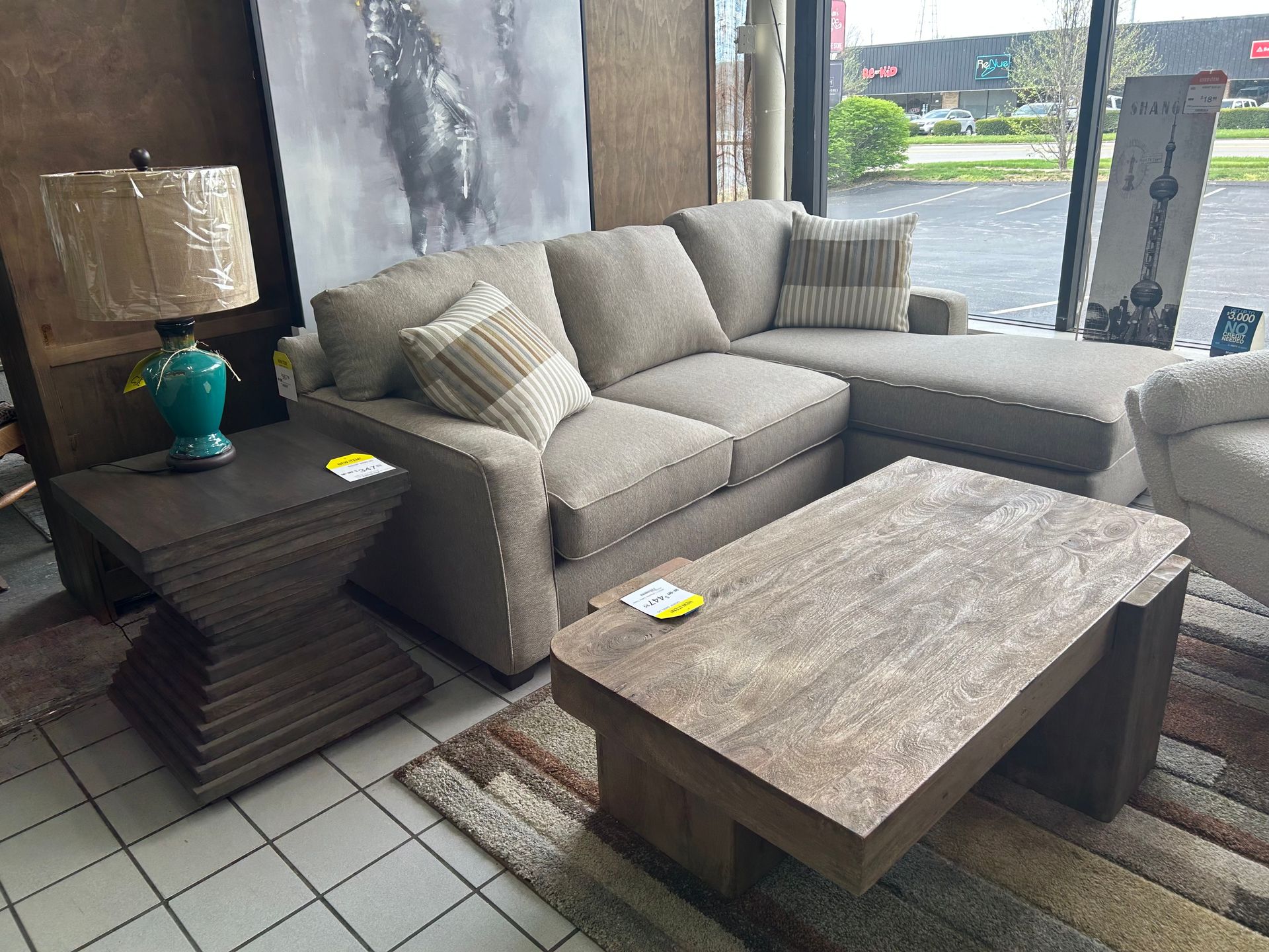 A beige sectional sofa, rustic wooden coffee table, and side table with a teal lamp in a furniture showroom.