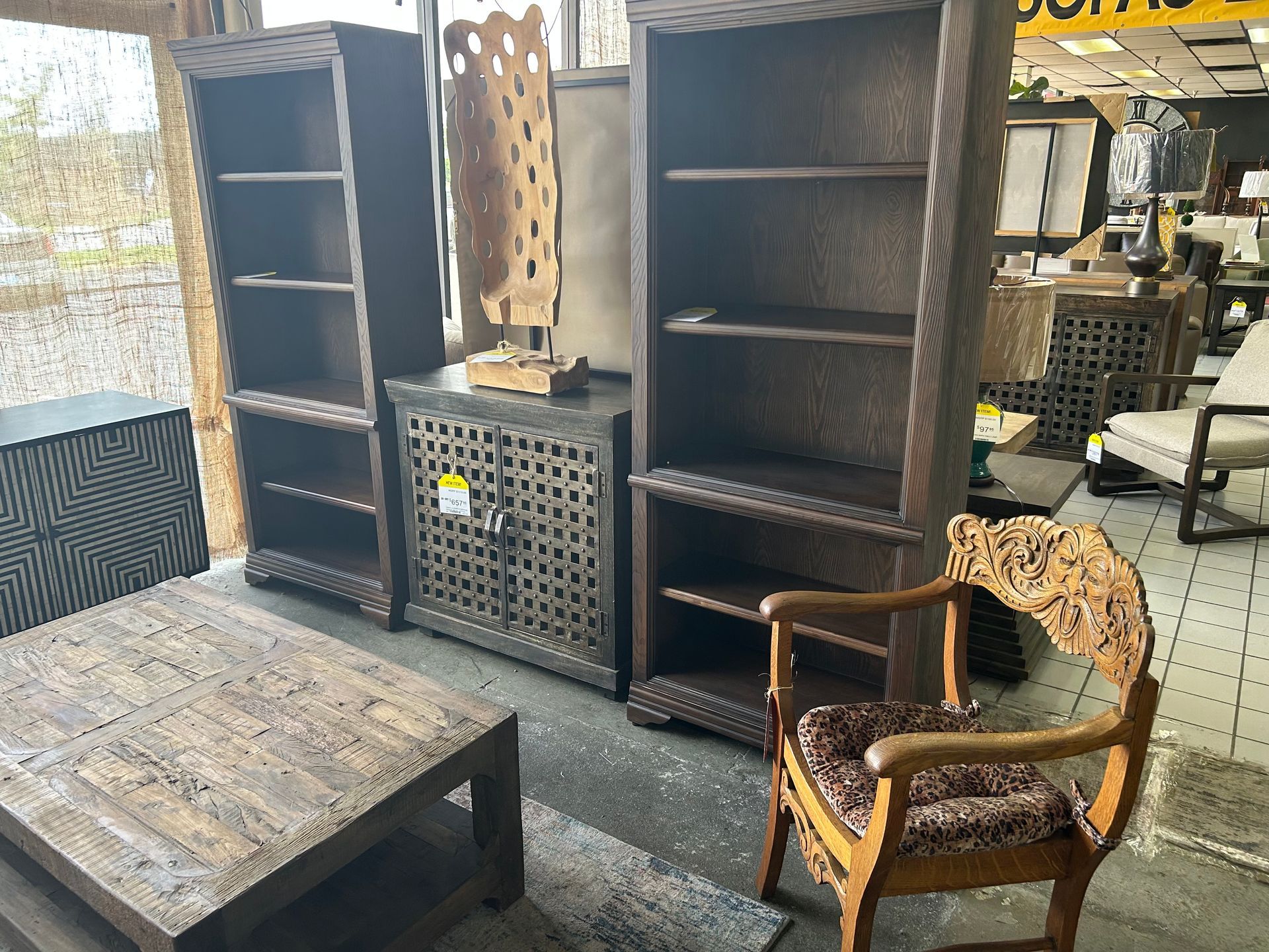 A furniture store display featuring dark wood bookshelves, a patterned cabinet, a rustic coffee table, and an ornate chair.