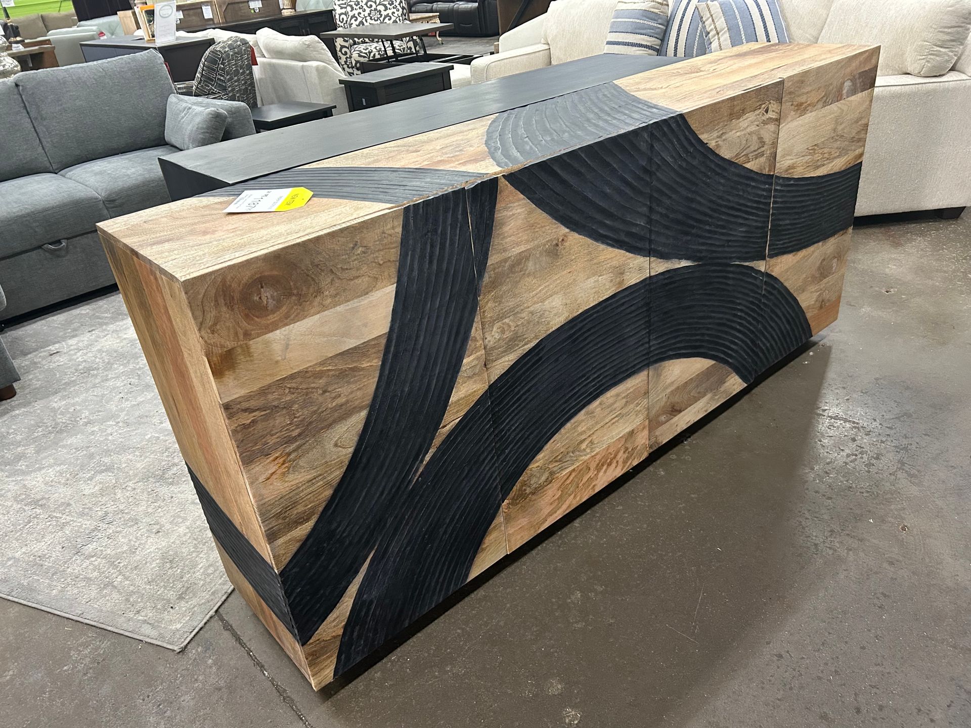 A light wood sideboard cabinet with bold, black circular textured patterns on the front, displayed in a furniture store.