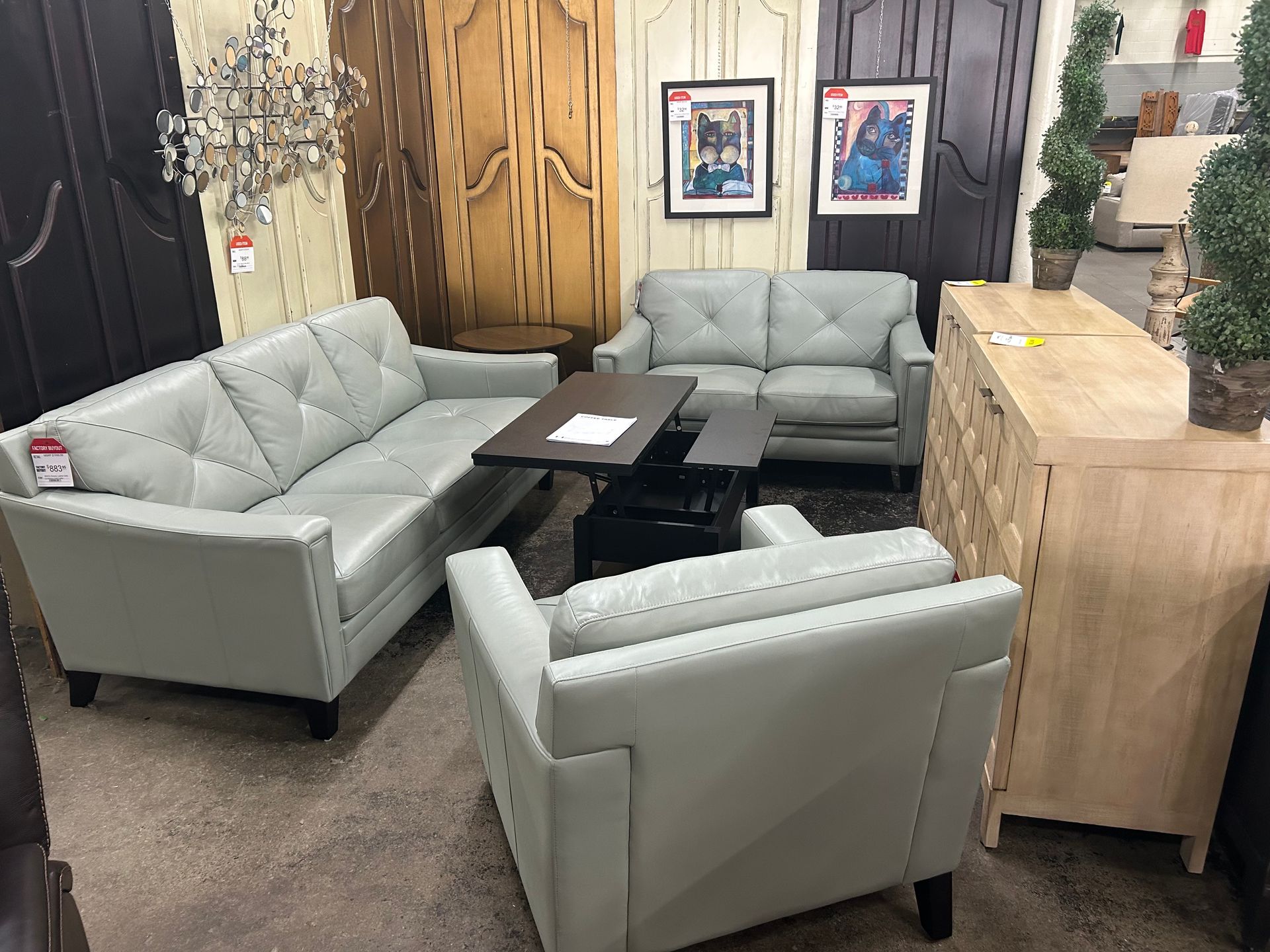 A showroom display featuring light blue leather furniture, including a sofa, loveseat, armchair, and wooden chest.