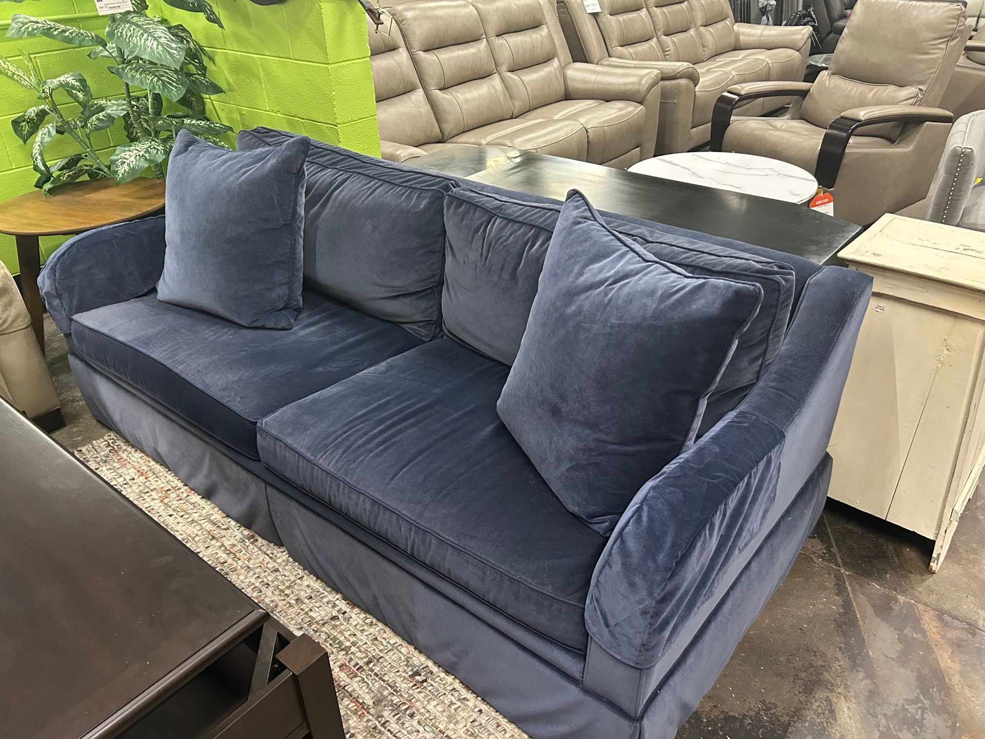 A navy blue fabric sofa with two matching throw pillows sits in a furniture showroom next to a light-colored side table.