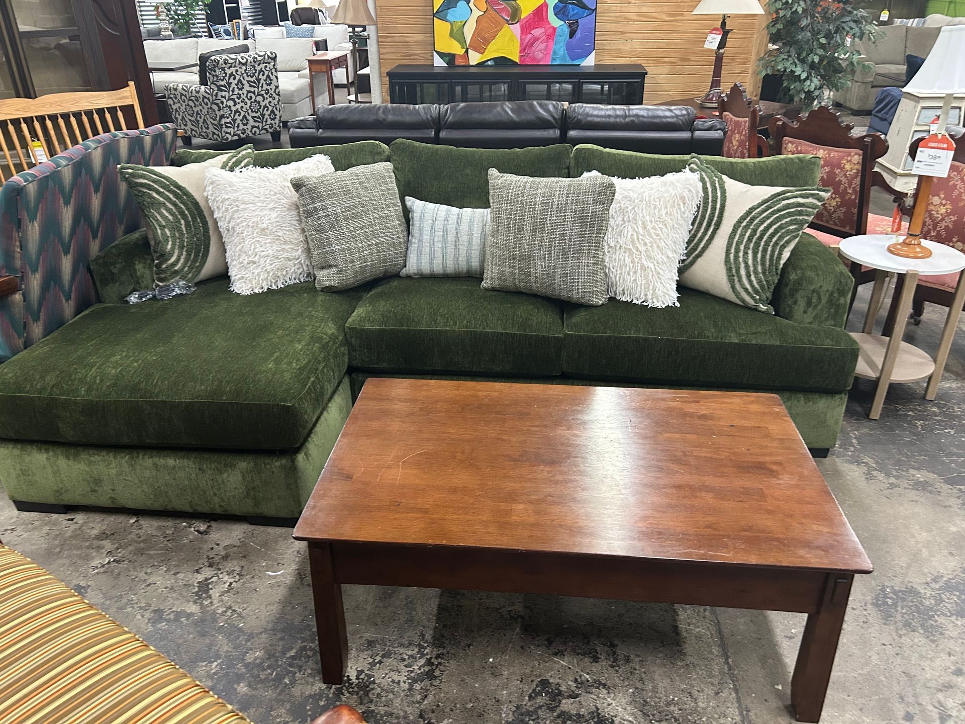 A dark green sectional sofa with textured throw pillows and a wooden coffee table in a furniture showroom.
