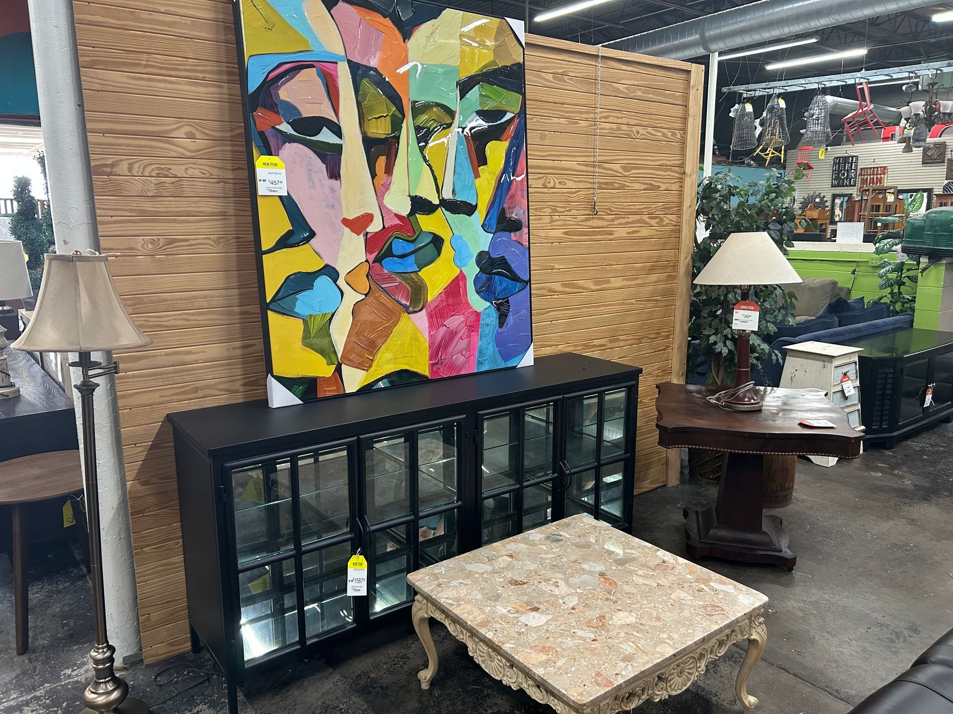 A modern abstract face painting hangs above a black glass cabinet, next to a lamp and a beige marble-topped coffee table.