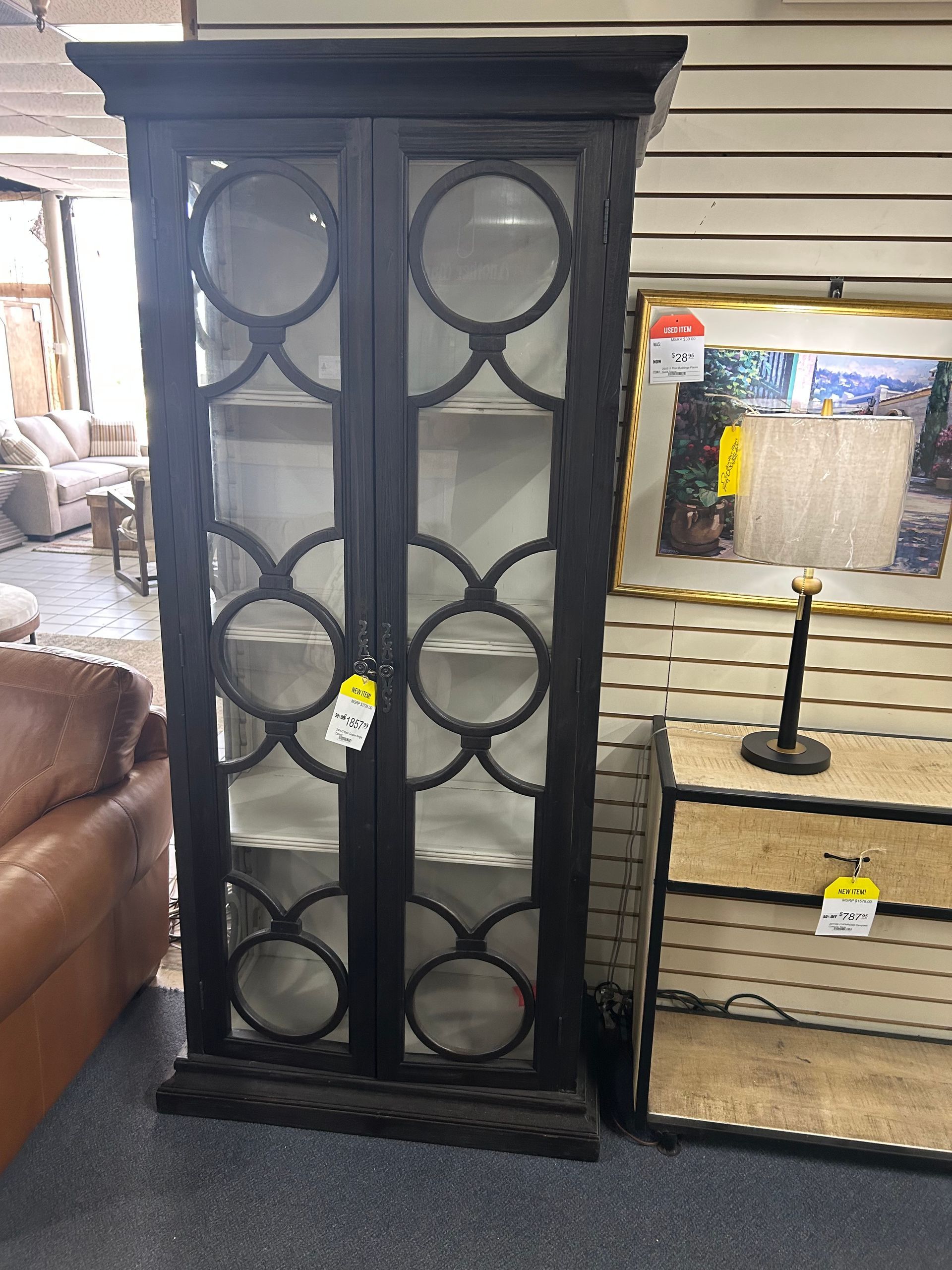 A tall, black display cabinet with glass doors featuring a repeating circular lattice design stands in a retail store.