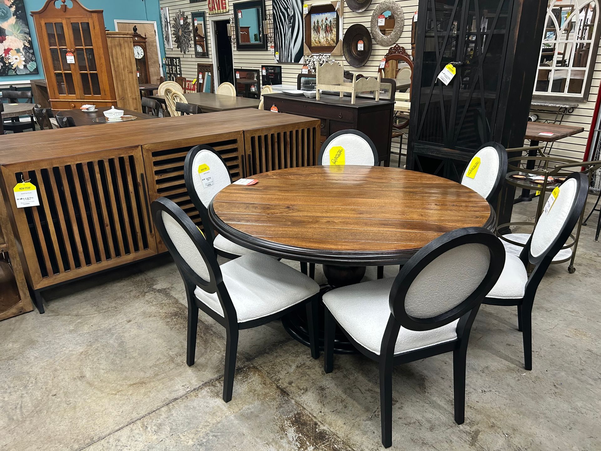 A round, wooden dining table with four black chairs featuring white upholstered oval backs and seats in a furniture store.