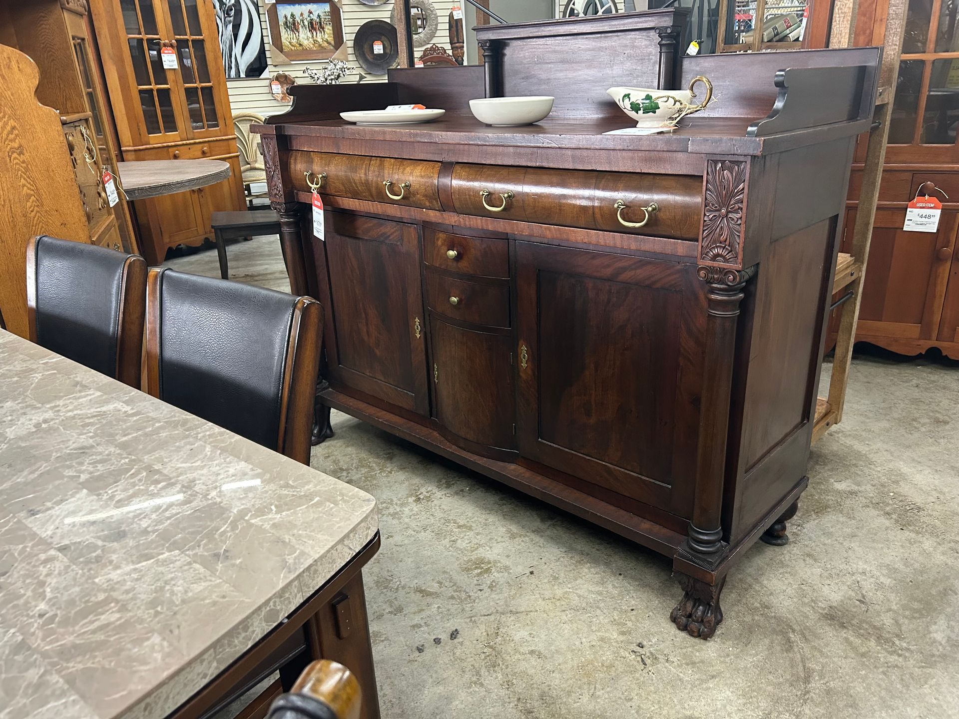 An ornate, dark wood antique sideboard with carved details and claw feet, displayed in a furniture store.