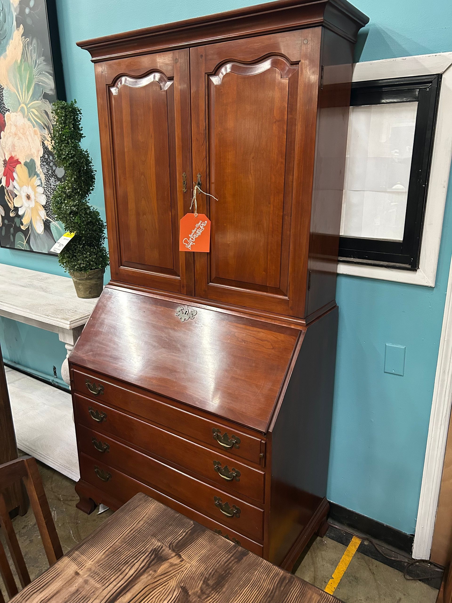 A wooden secretary desk with a hutch, featuring upper cabinet doors, a drop-down writing surface, and three lower drawers.