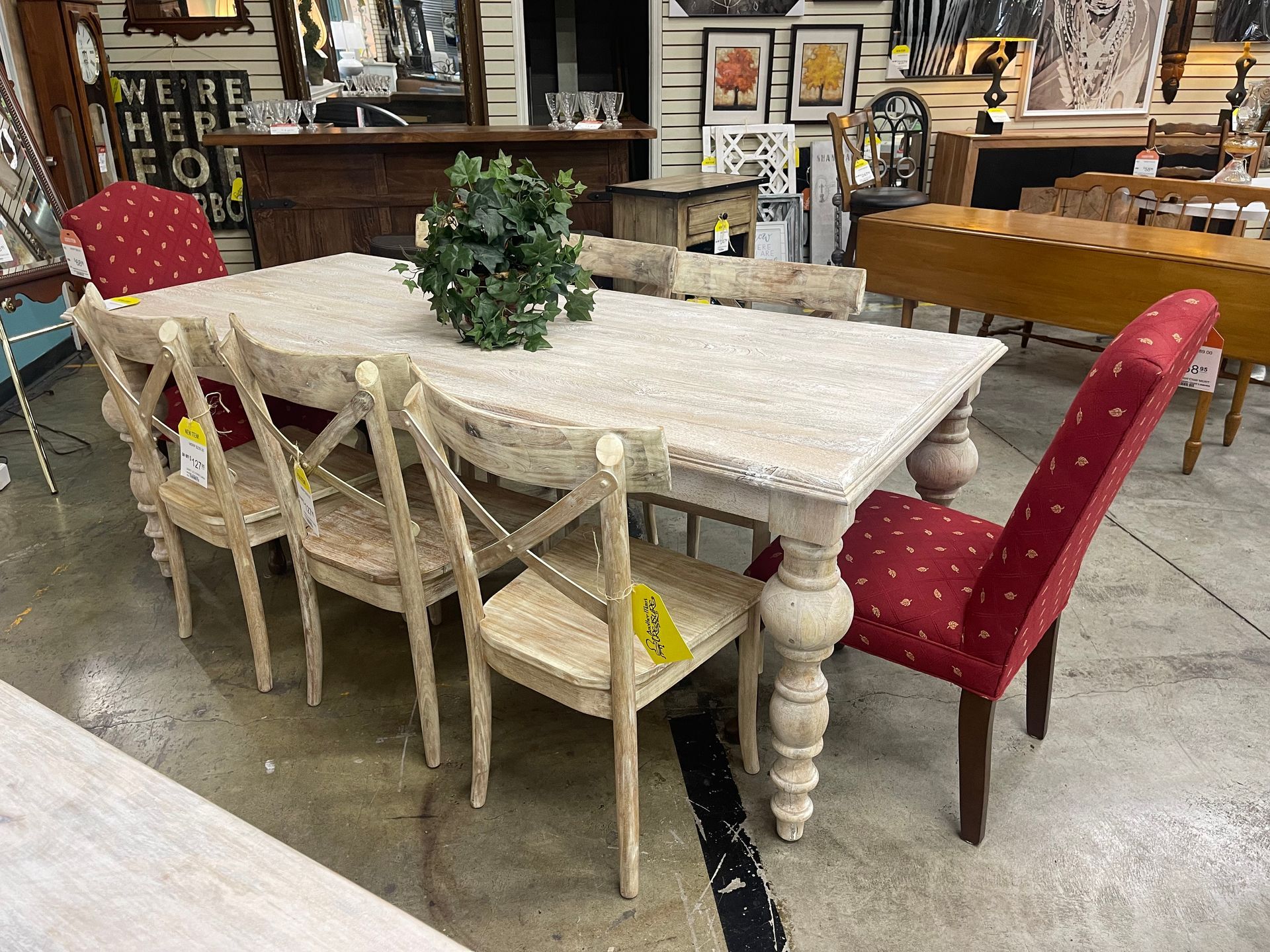 A dining set with a distressed white wooden table and chairs, including two red patterned chairs, in a showroom.