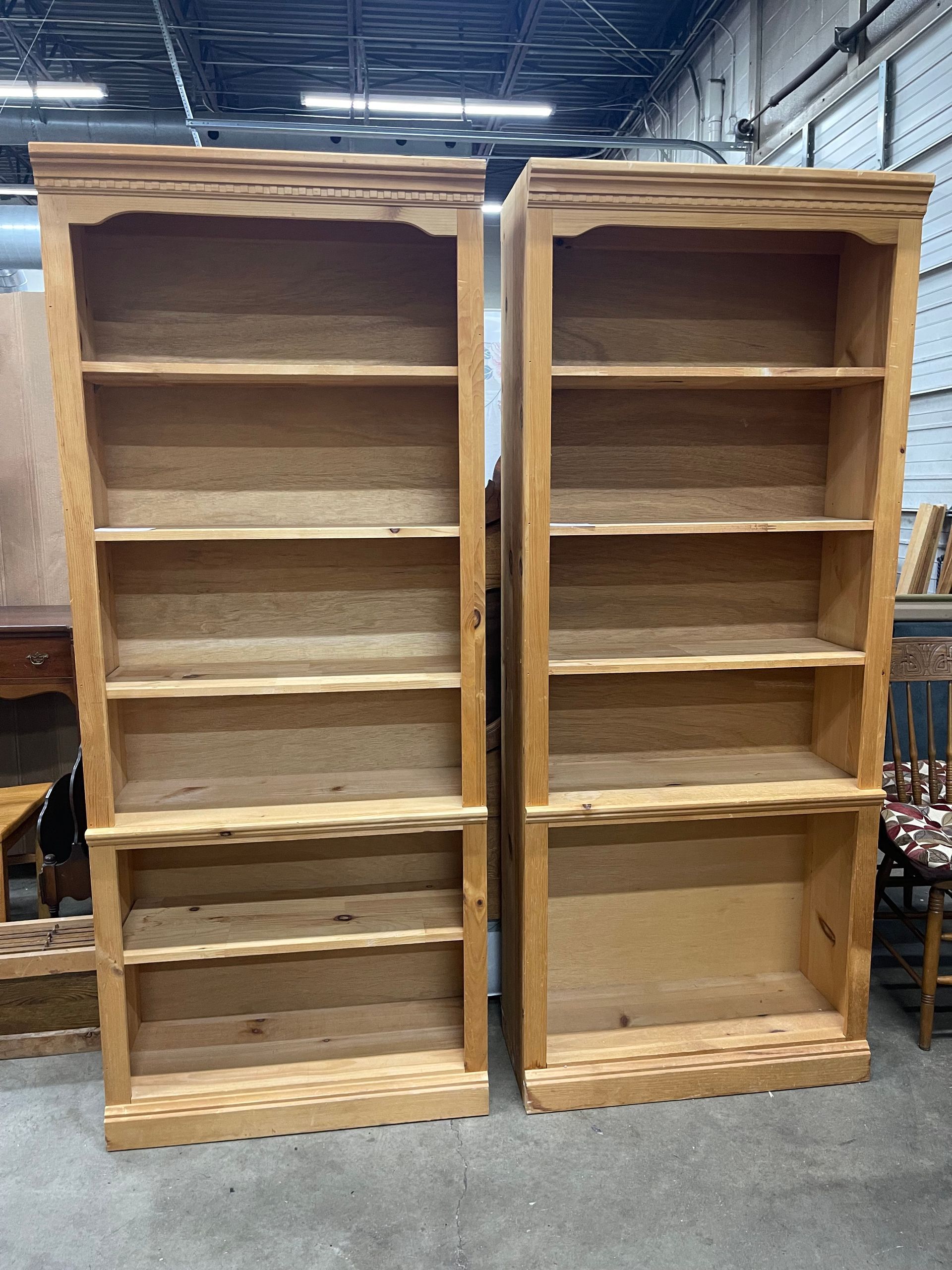 Two tall, light wood bookshelves with decorative wavy trim edges, standing side-by-side in a warehouse or workshop.