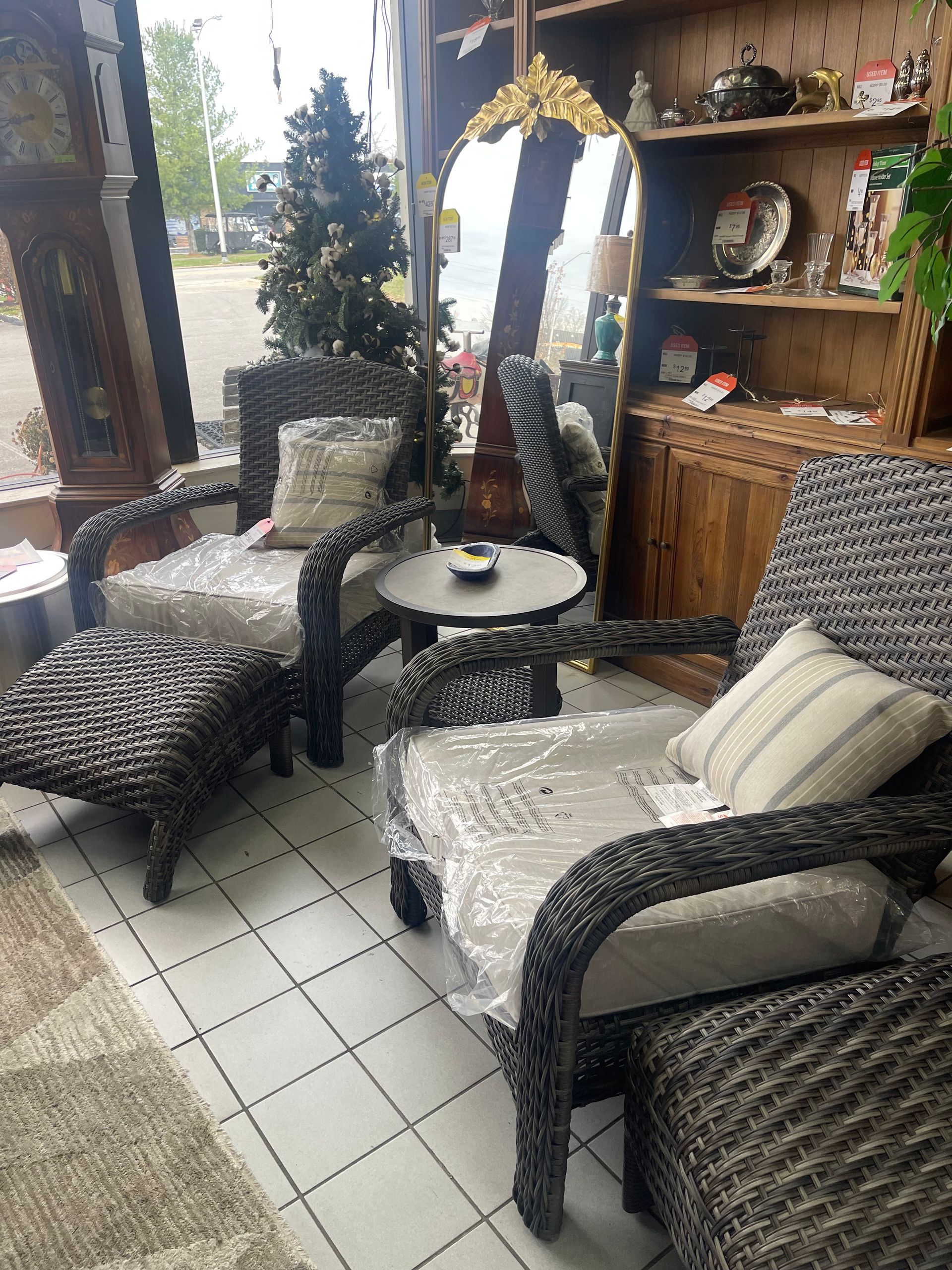 A small seating area with two wicker armchairs, matching ottomans, and a round side table on a white tiled floor.