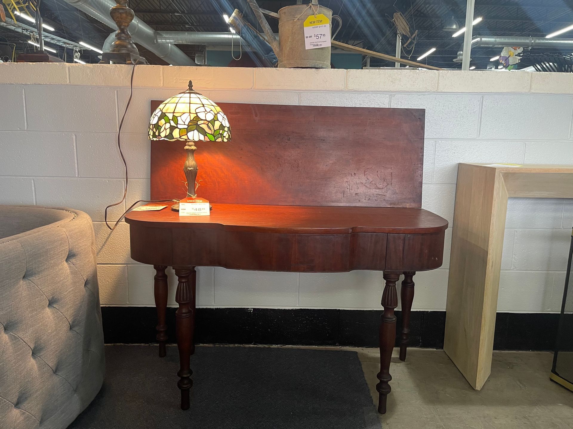A wooden console table with a stained-glass lamp sits in a room with white cinder block walls.