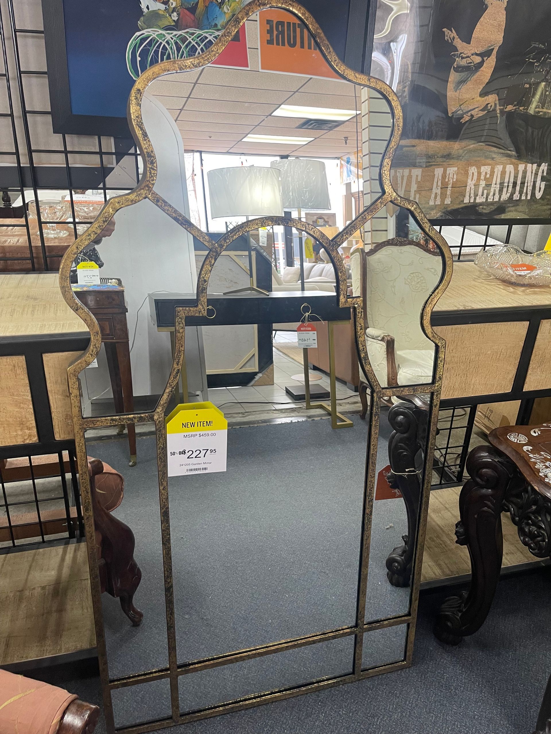 A tall, ornate gold-framed mirror with a Moroccan-style arched top, displayed in a store with furniture in the background.