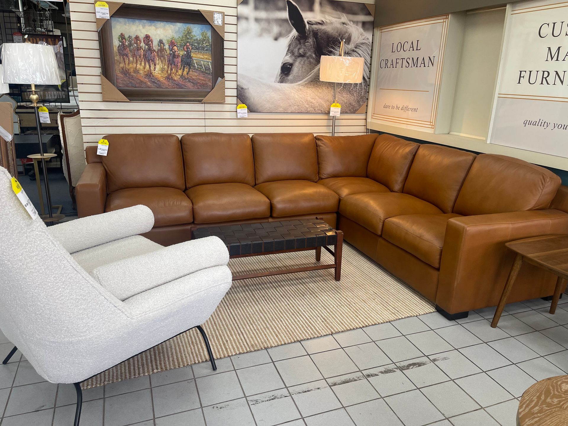 A tan leather sectional sofa with a white textured armchair and a coffee table on a rug in a furniture showroom.