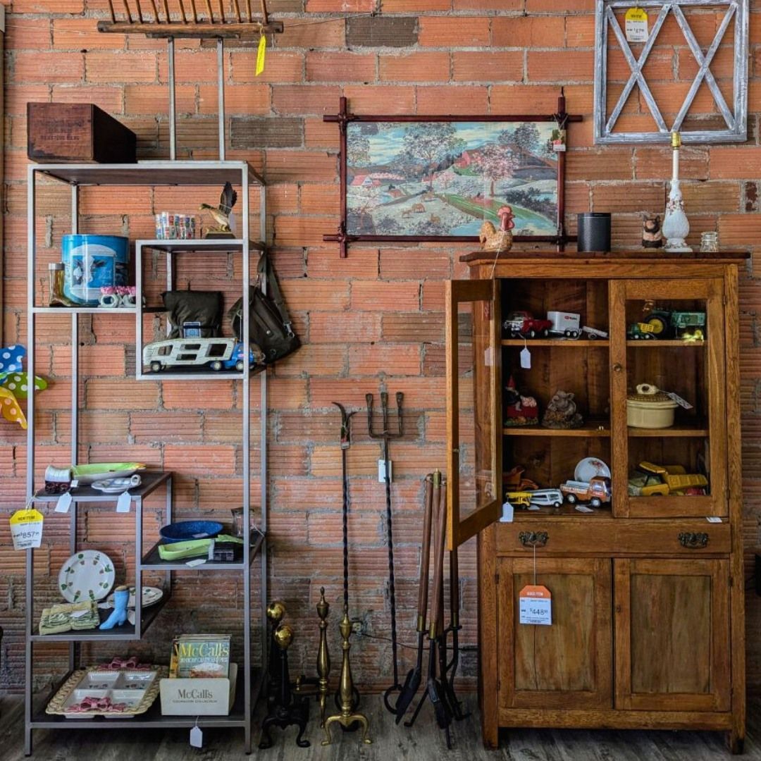An antique shop display with a metal shelving unit, a wood cabinet, and vintage home goods against a brick wall.