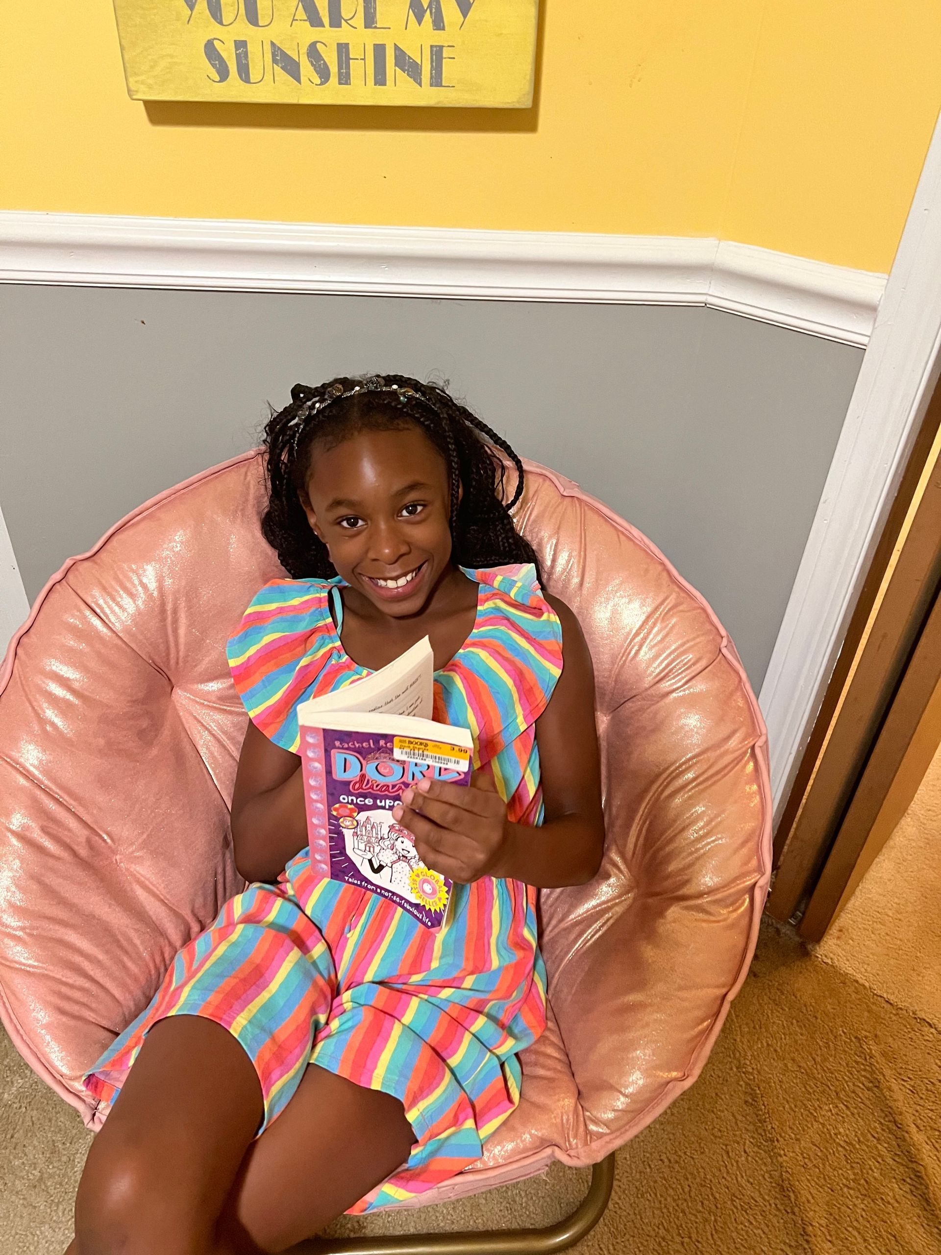 A young girl is sitting in a chair reading a book.