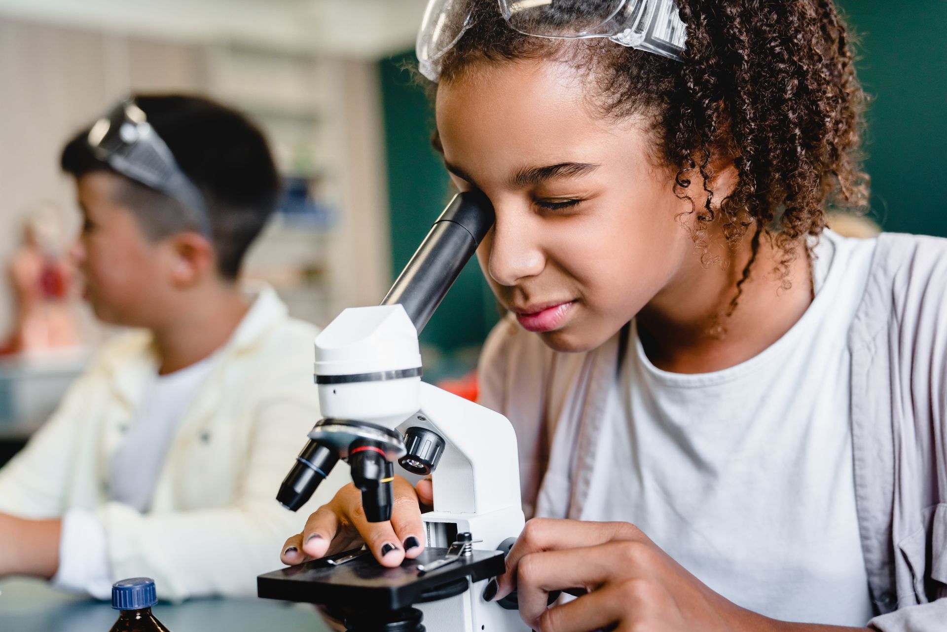 A girl is looking through a microscope in a lab.