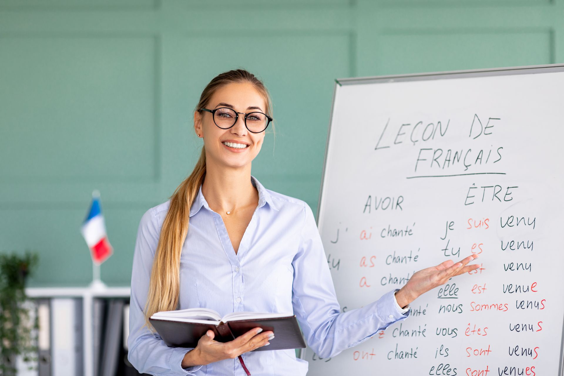 A woman is standing in front of a whiteboard teaching french.