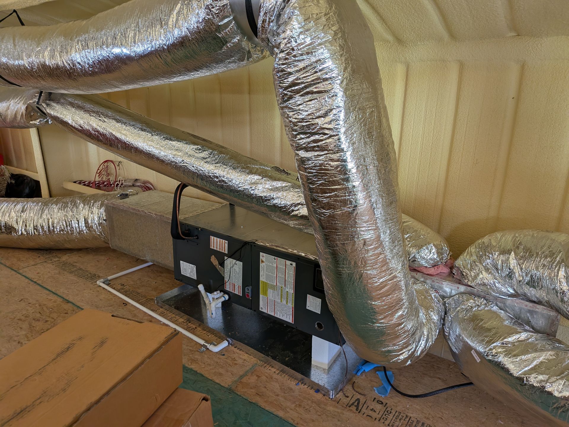 HVAC unit with silver ductwork in an attic space. Insulation visible on the walls.
