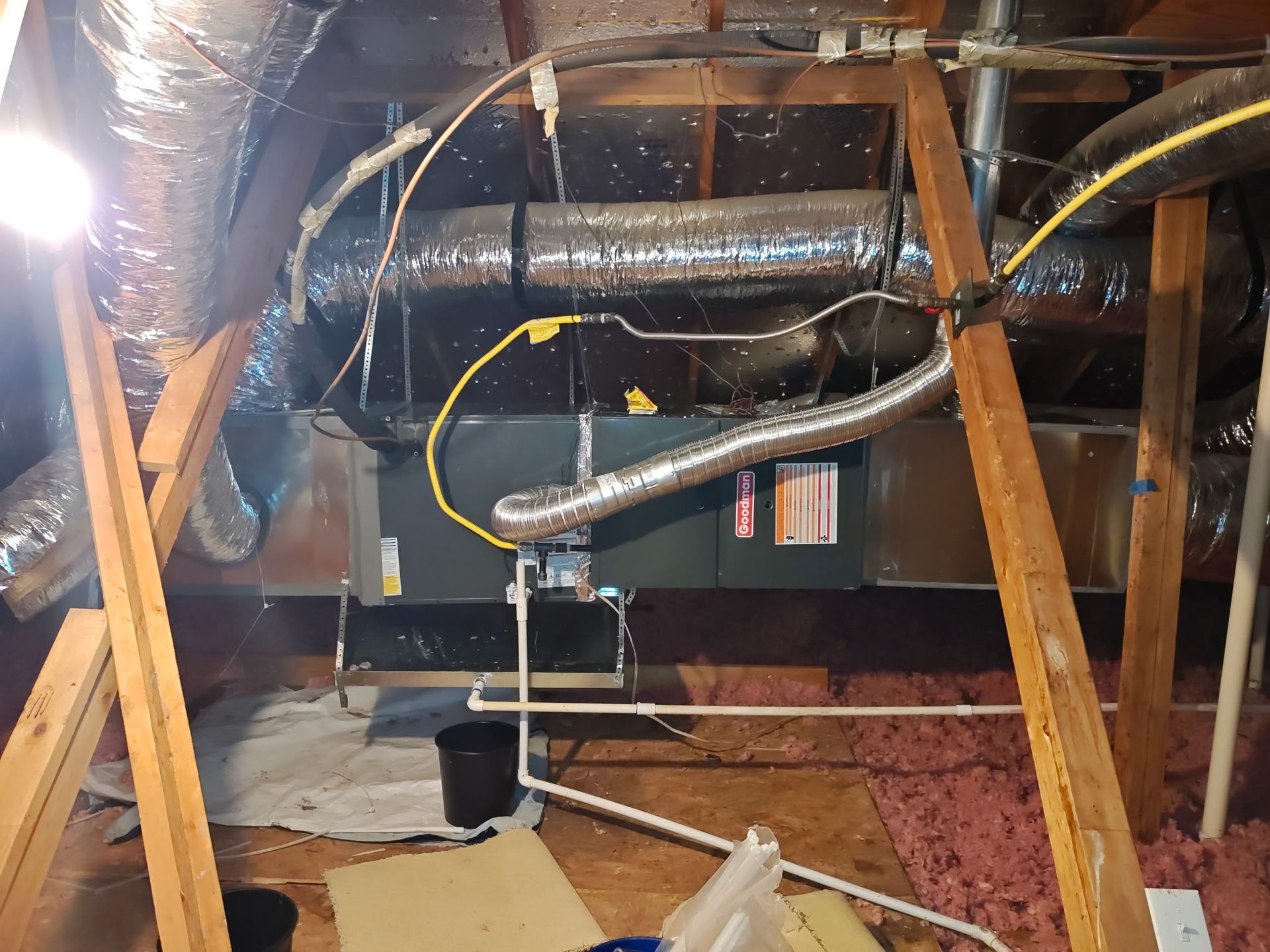 An HVAC unit in an attic. Ductwork, electrical wiring, and wooden support beams are visible.