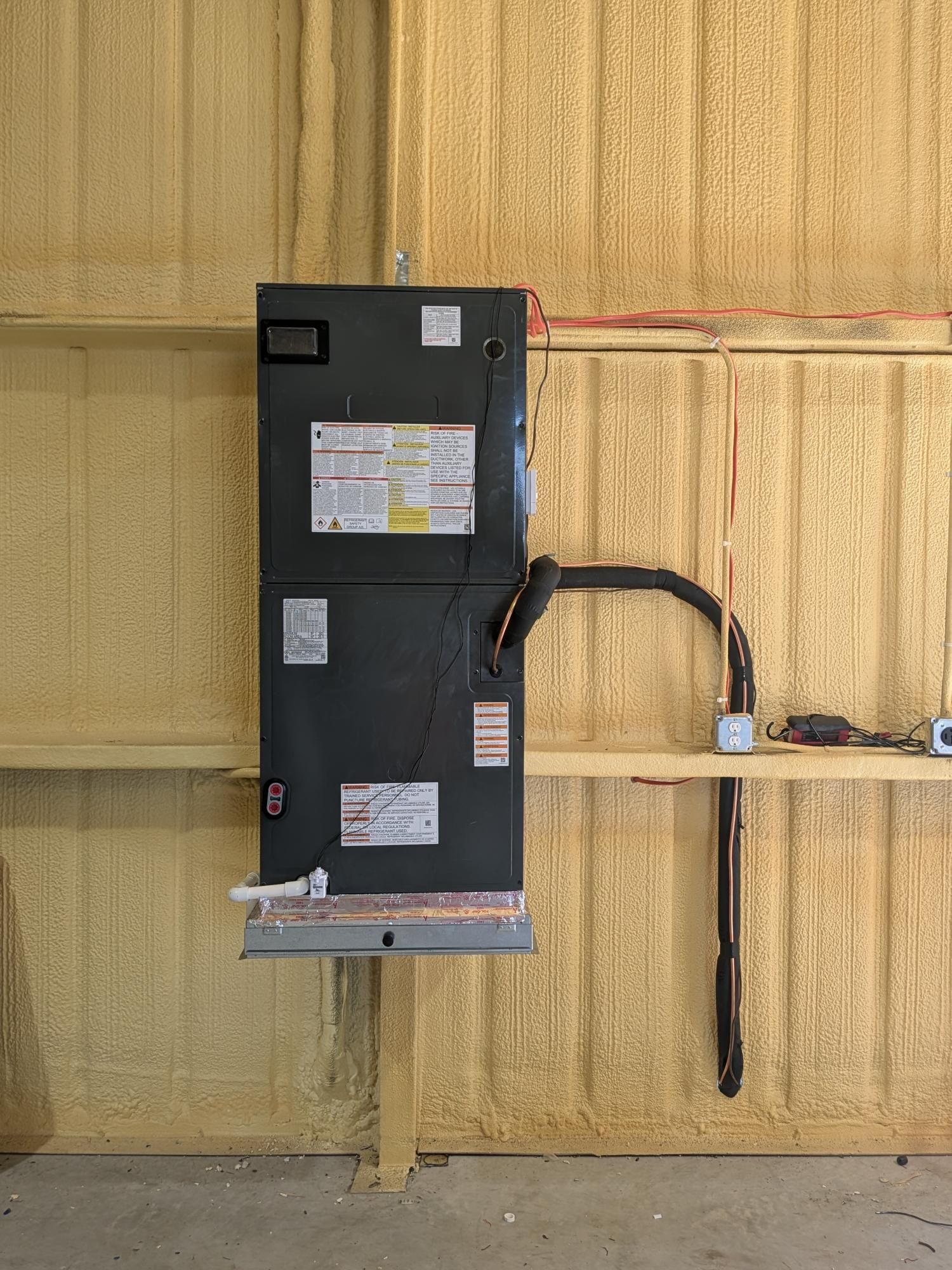 HVAC unit mounted on a support beam in a building. Copper pipes and electrical wiring are visible.