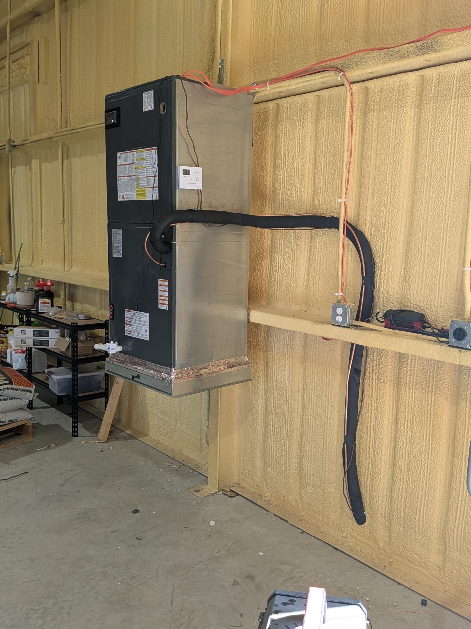 HVAC unit mounted on a wall with ductwork, electrical conduit, and exposed insulation.