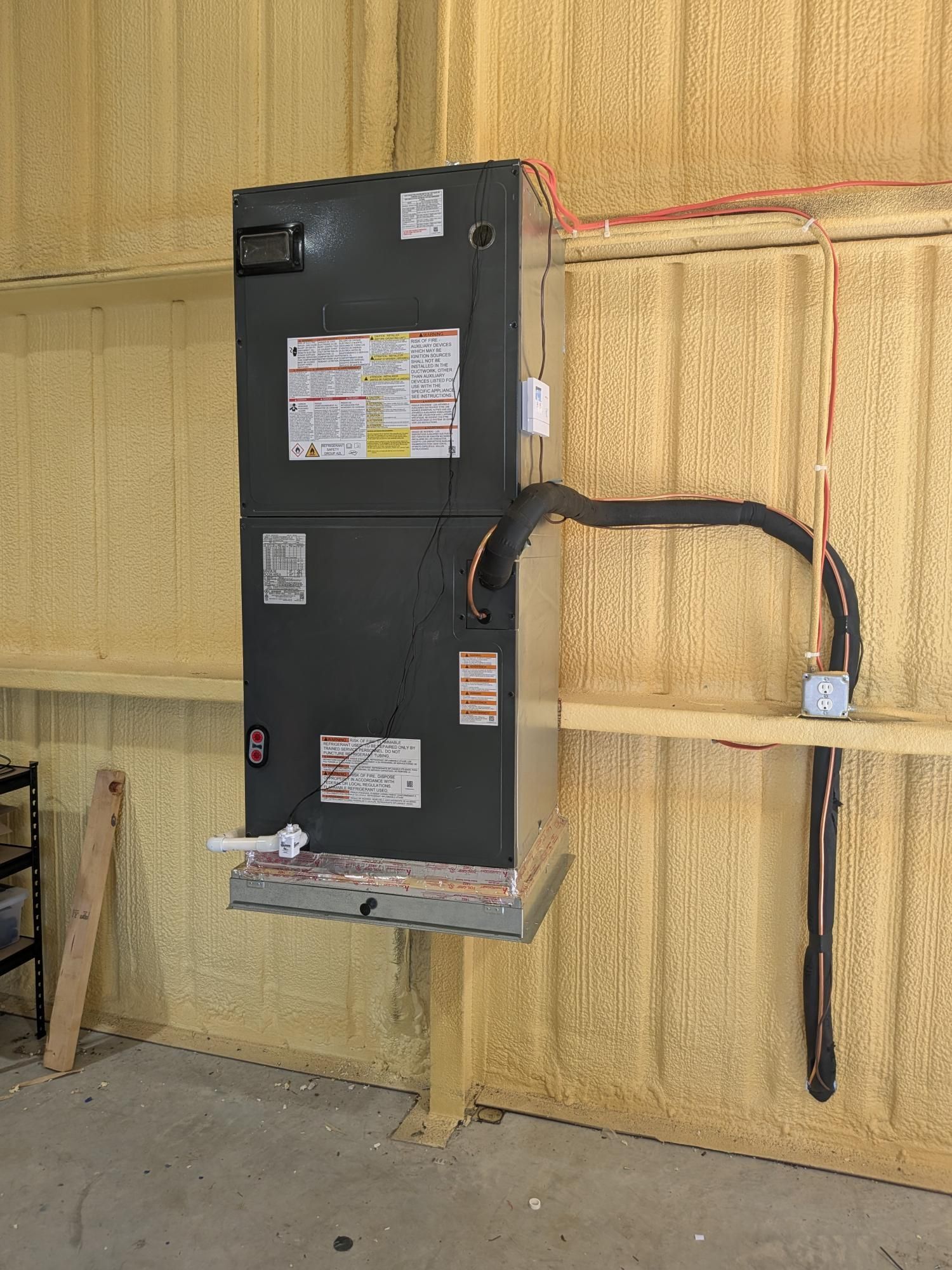 HVAC unit mounted on a wooden shelf on a wall, with pipes and electrical wiring.