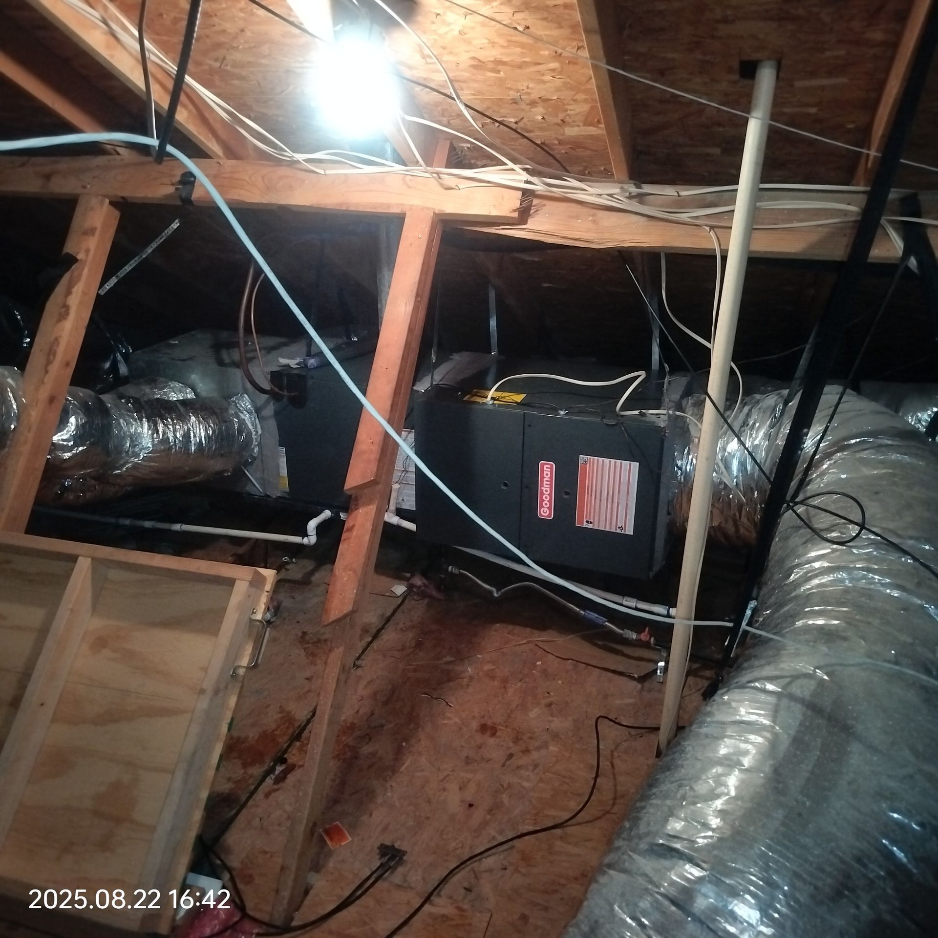 HVAC unit and ductwork in an attic. Electrical wires and wooden framing visible.
