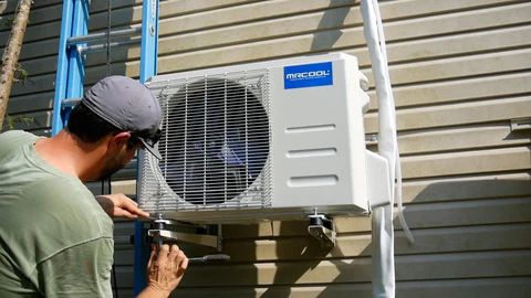 Man installing an AC unit on a wall, using a ladder.
