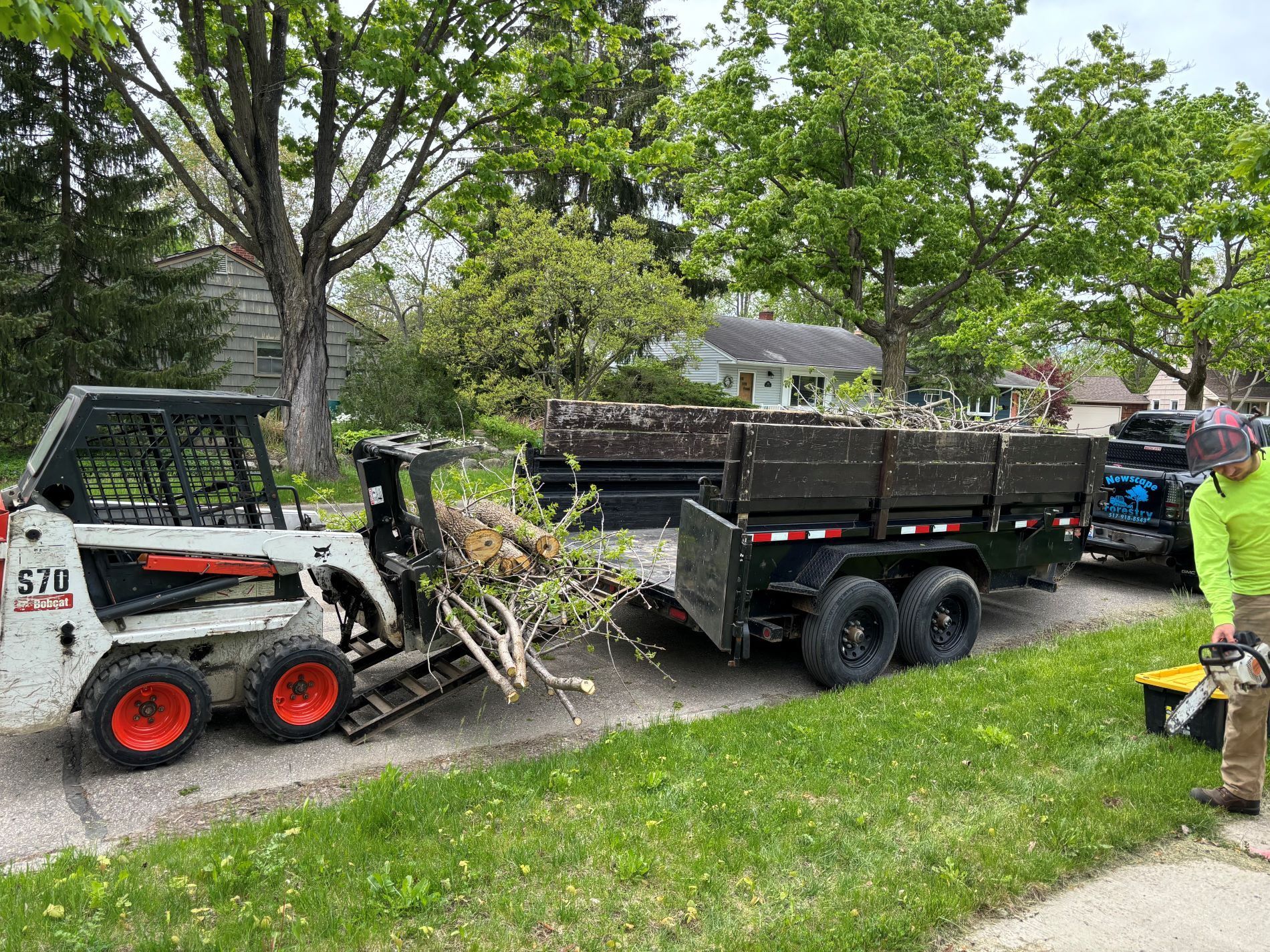 A man is standing next to a bulldozer pulling a trailer full of branches.