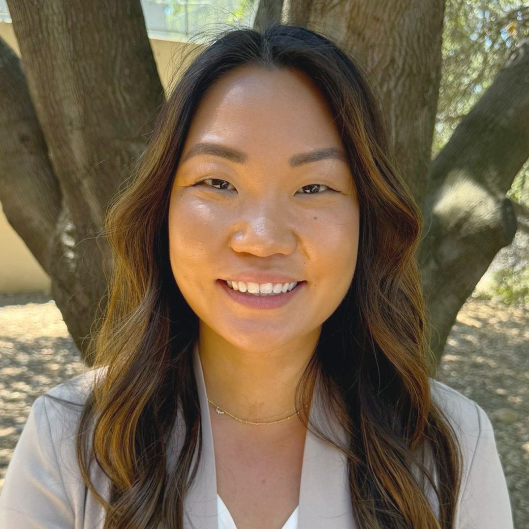 A woman is smiling for the camera in front of a tree.