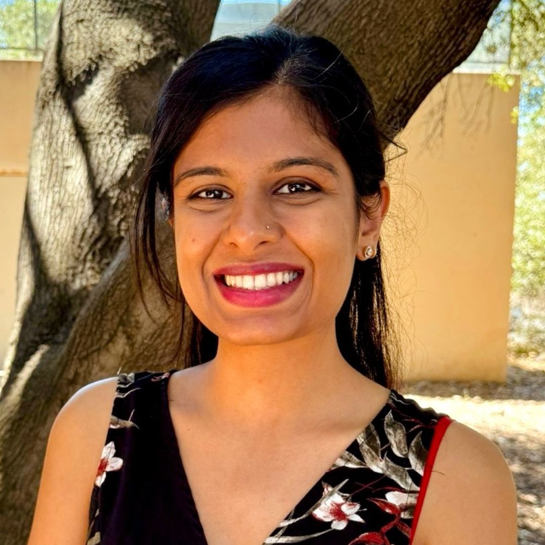 A woman is smiling for the camera in front of a tree