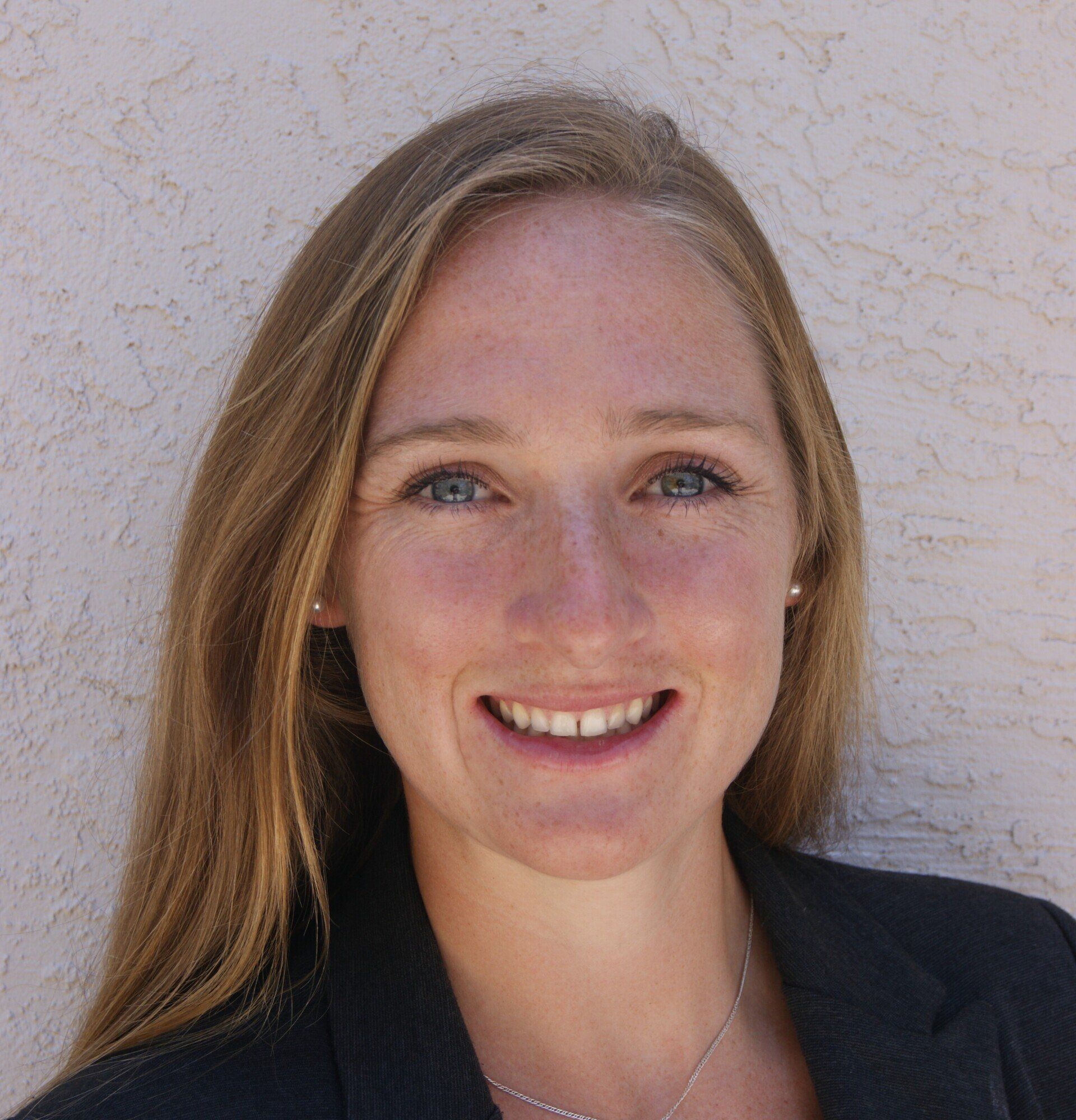 A woman with long blonde hair is smiling and wearing a black jacket