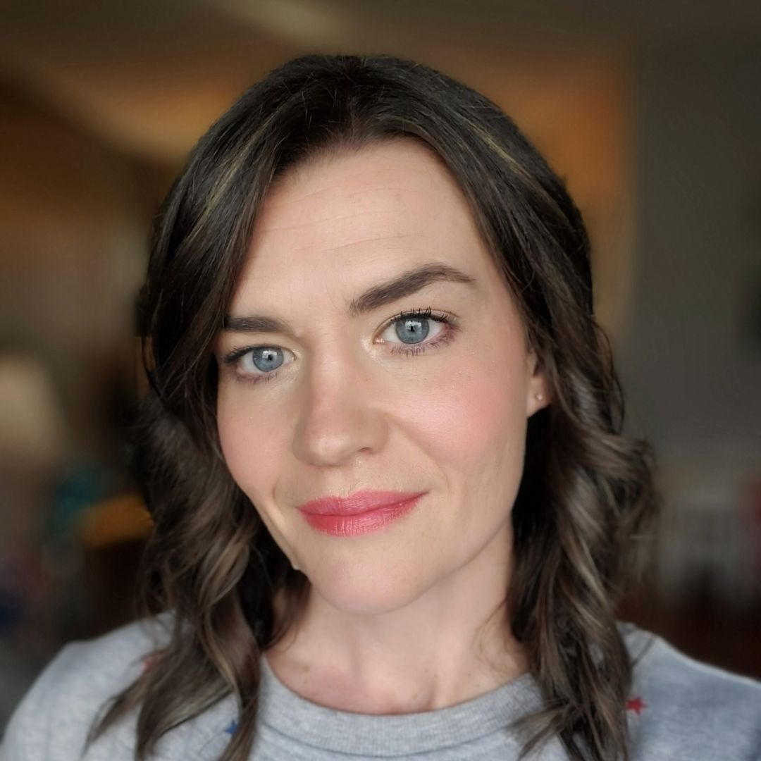 A woman with long hair and blue eyes is smiling for the camera.