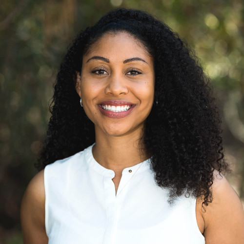 A woman in a suit is smiling in front of a tree.