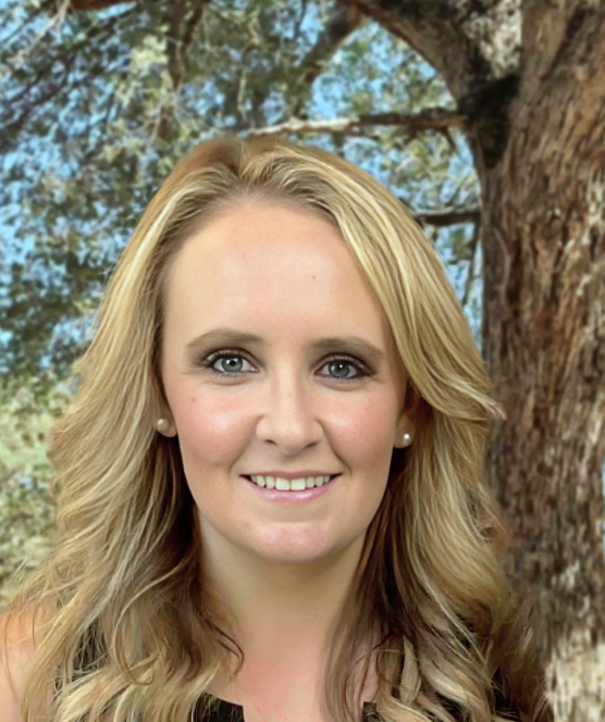 A woman with blonde hair is smiling in front of a tree.