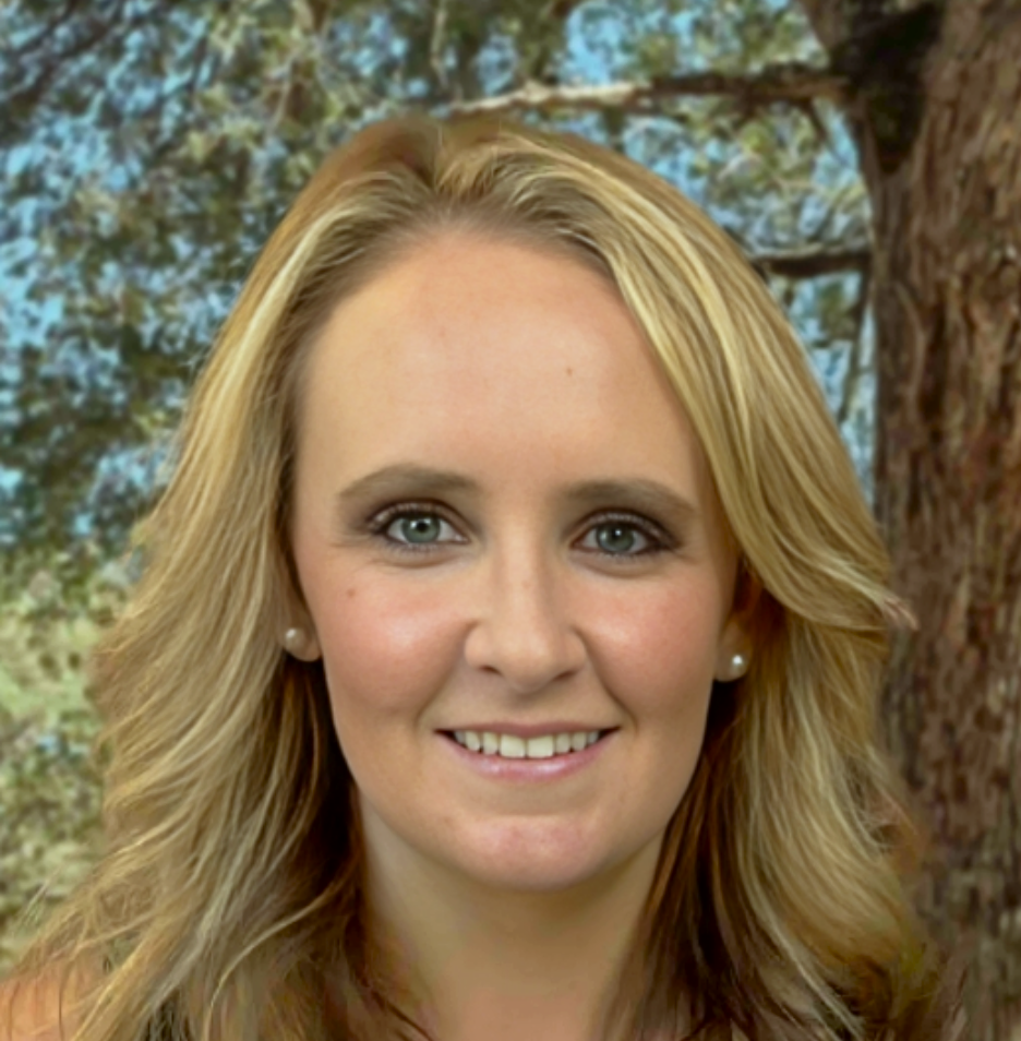 A woman with blonde hair is smiling in front of a tree