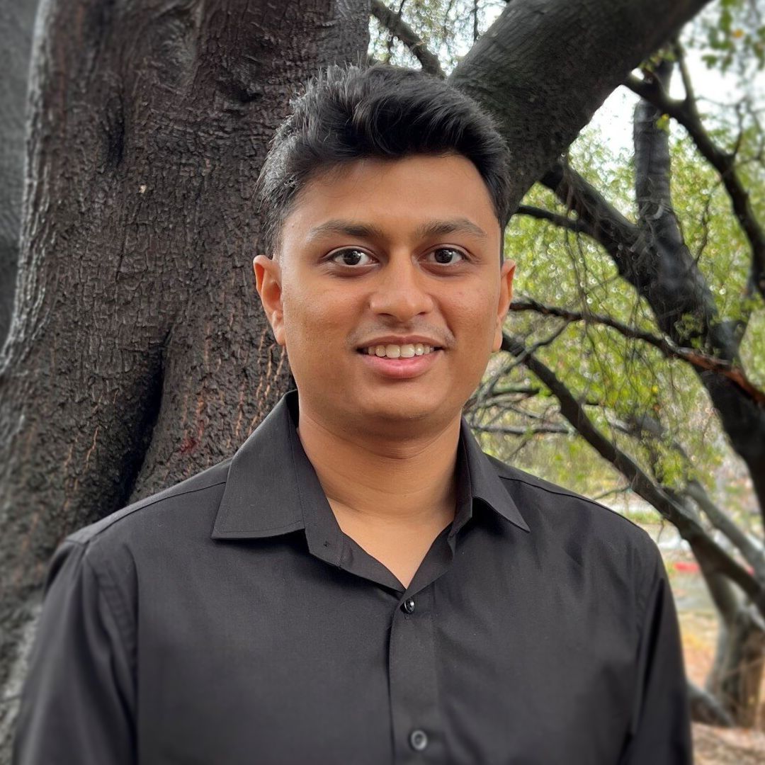 A man in a black shirt is standing in front of a tree.