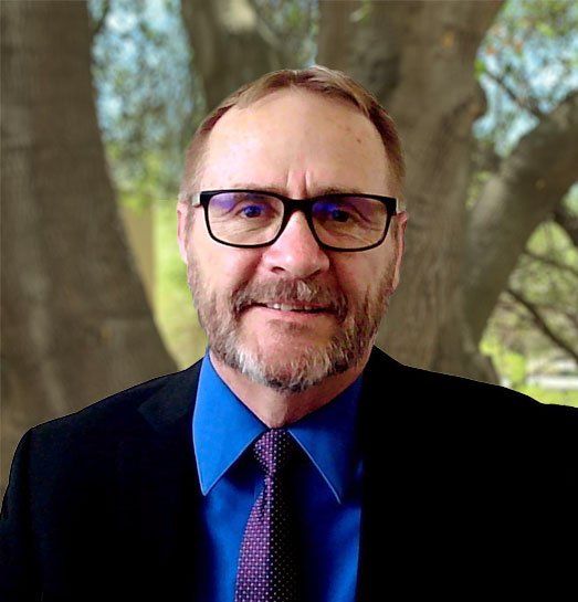 A man with a beard and glasses is wearing a blue shirt and tie.