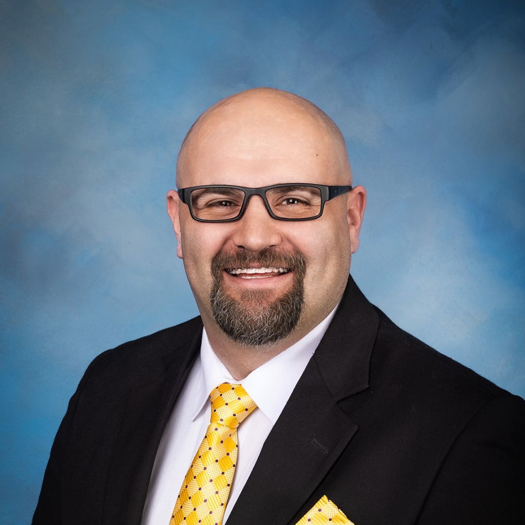 A bald man wearing glasses and a yellow tie
